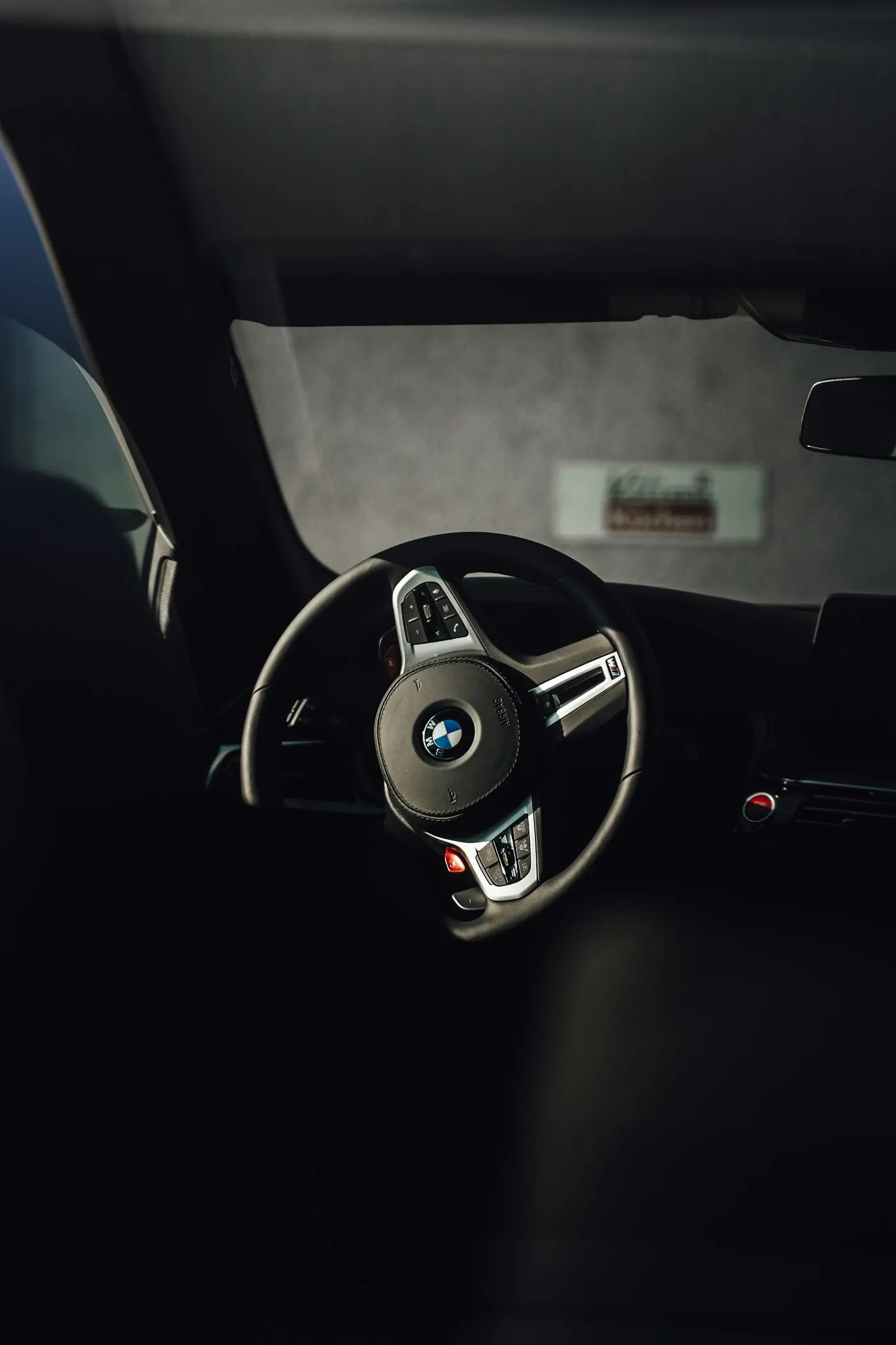BMW M Sport vairas su raudonu M mygtuku tamsiame salone